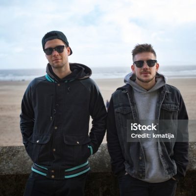Two Young Men Standing By a Sandy Beach.