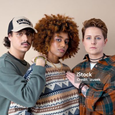 Black and white young women and young man standing in row and looking at camera. Studio shot, beige background.