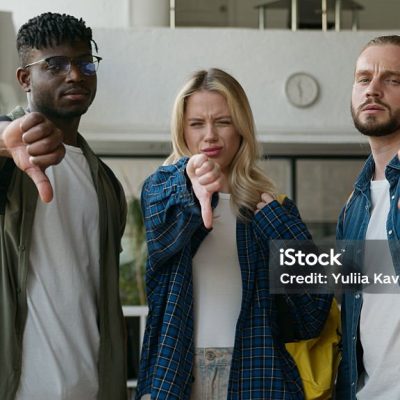 Three multiracial friends diversity students showing thumbs down negative dissatisfied bad dislikes looking at camera in university corridor hall together studying education problem unwell attitude. High quality 4k footage